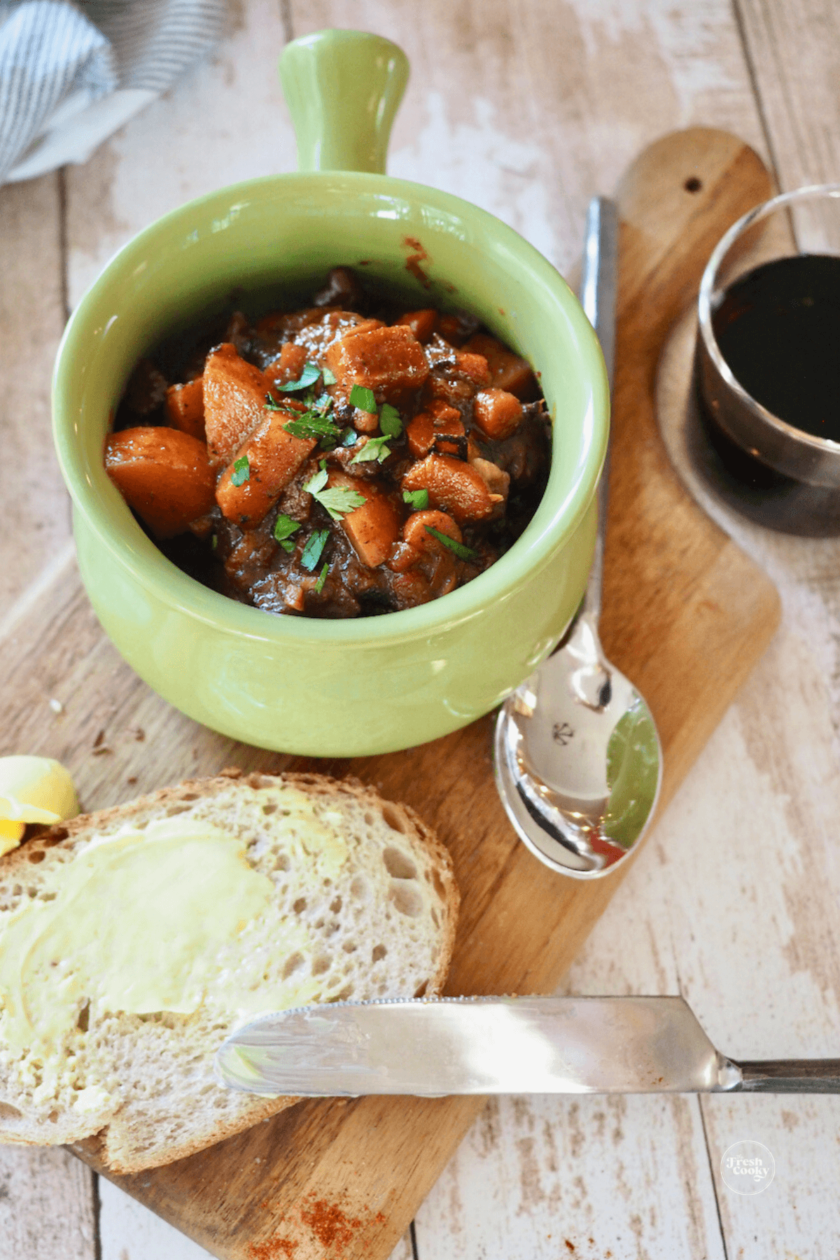 Small handled bowl filled with rich German goulash soup, on a breadboard with a slice of buttered rye bread.