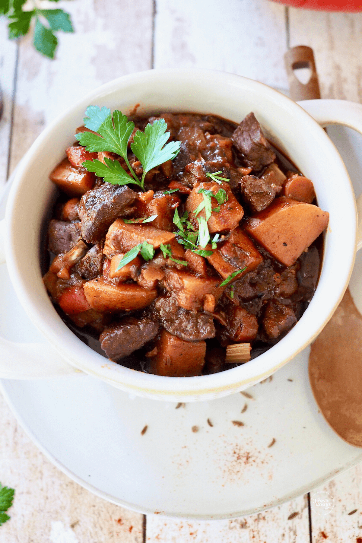 Large bowl of German goulash soup with caraway seeds, paprika and garnished with parsley.