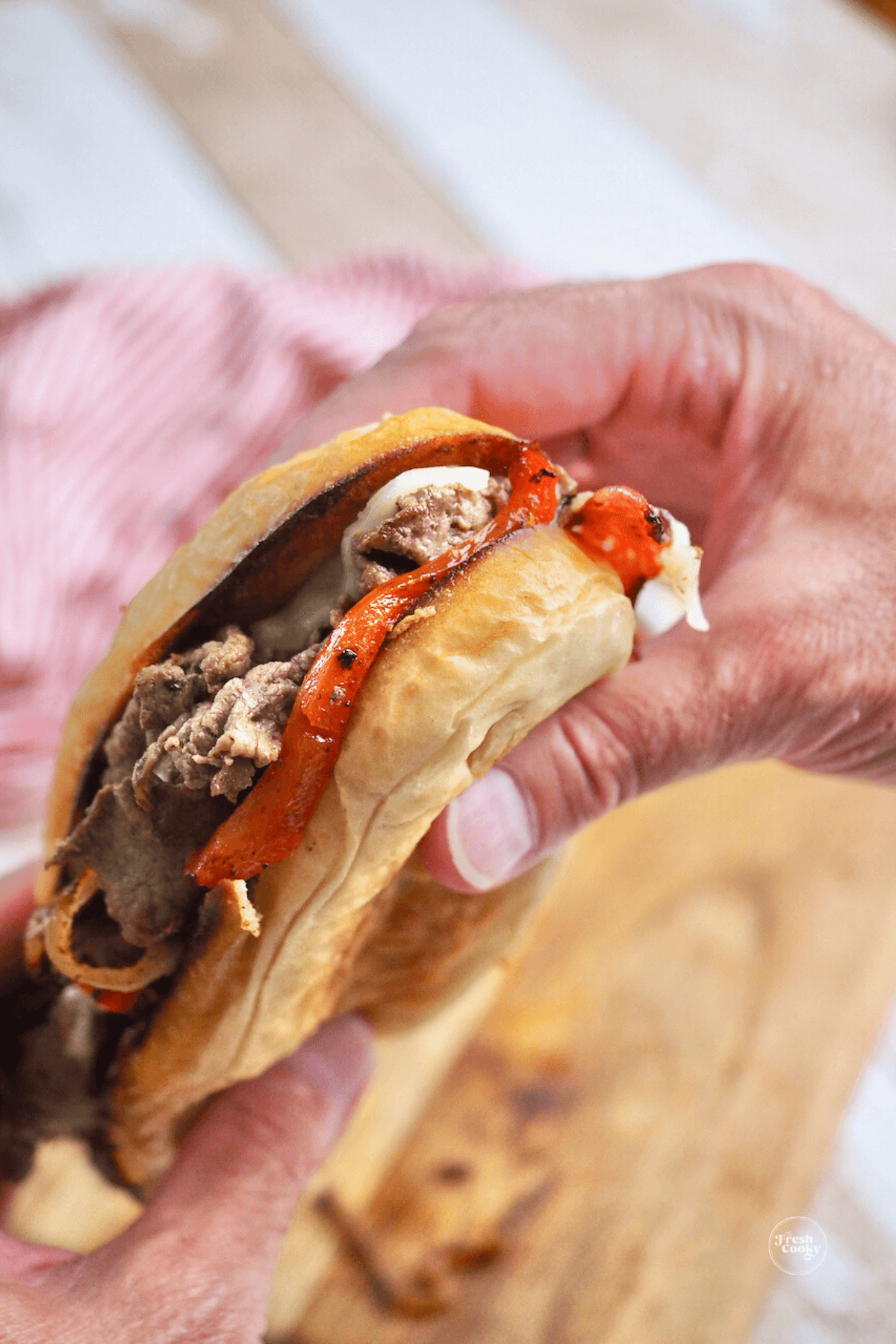 Hands holding steak bomb sandwich with melty cheese.