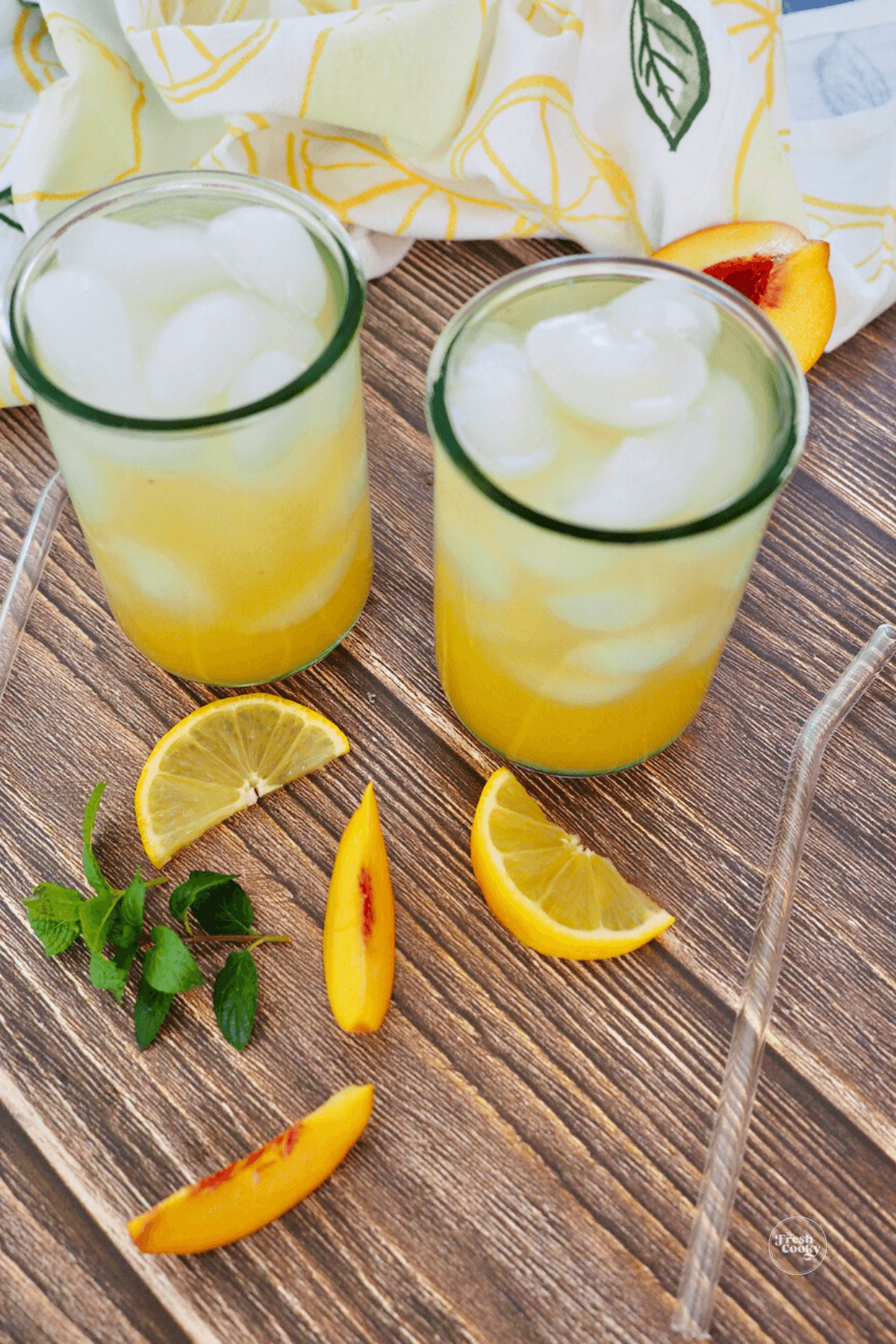 Two tall glasses filled with peach green tea lemonade with fresh peaches, lemon and mint. 