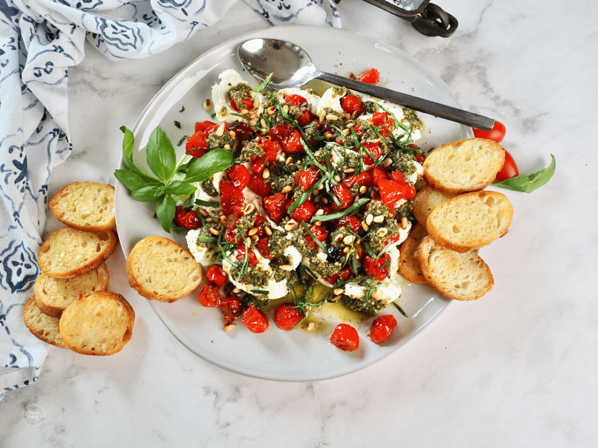 Burrata cheese, pesto and roasted tomatoes on plate with crostini for scooping.