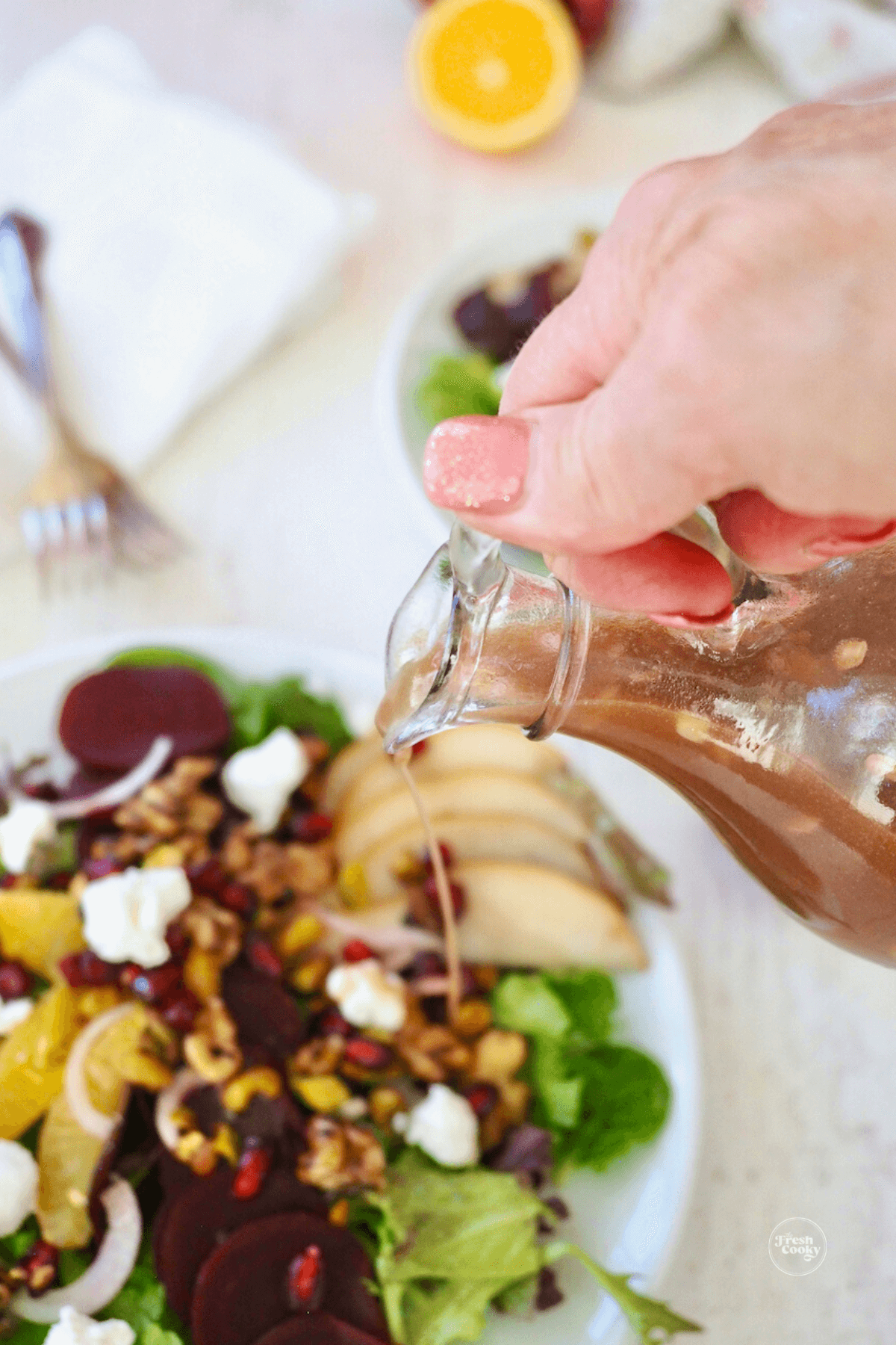 Hand pouring pomegranate vinaigrette onto pretty holiday salad.