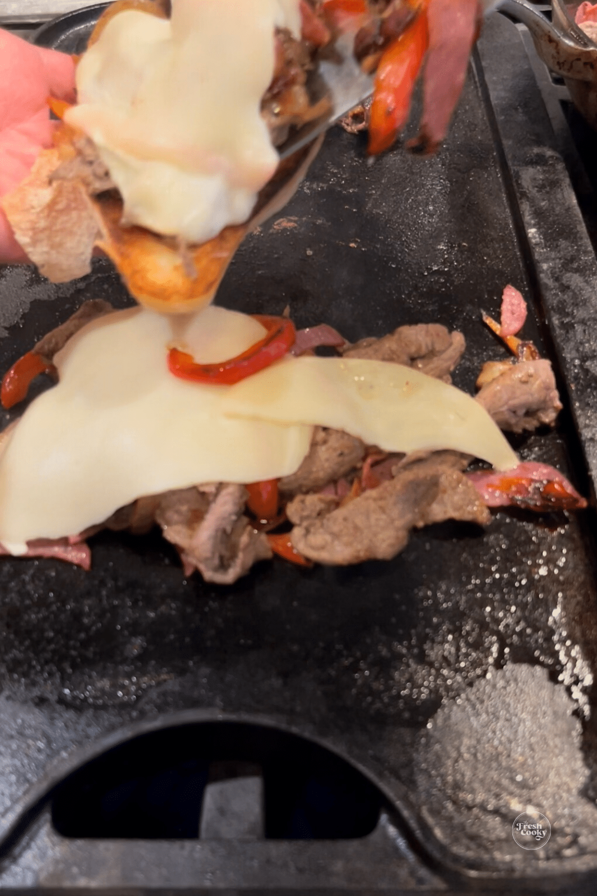 Steak mixture on griddle topped with cheese that is melting. 