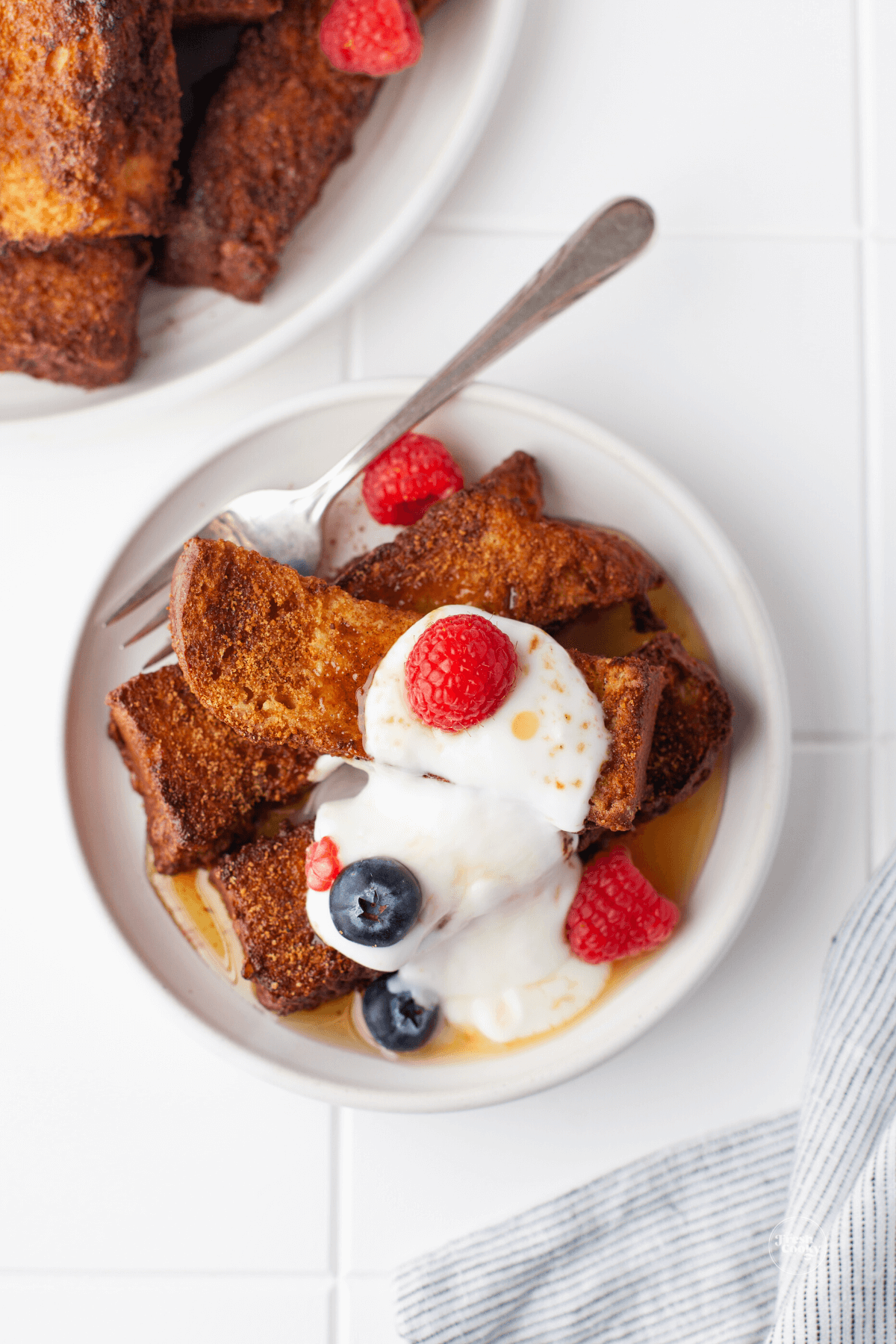 French toast sticks on plate with fork, maple syrup and cream and berries.