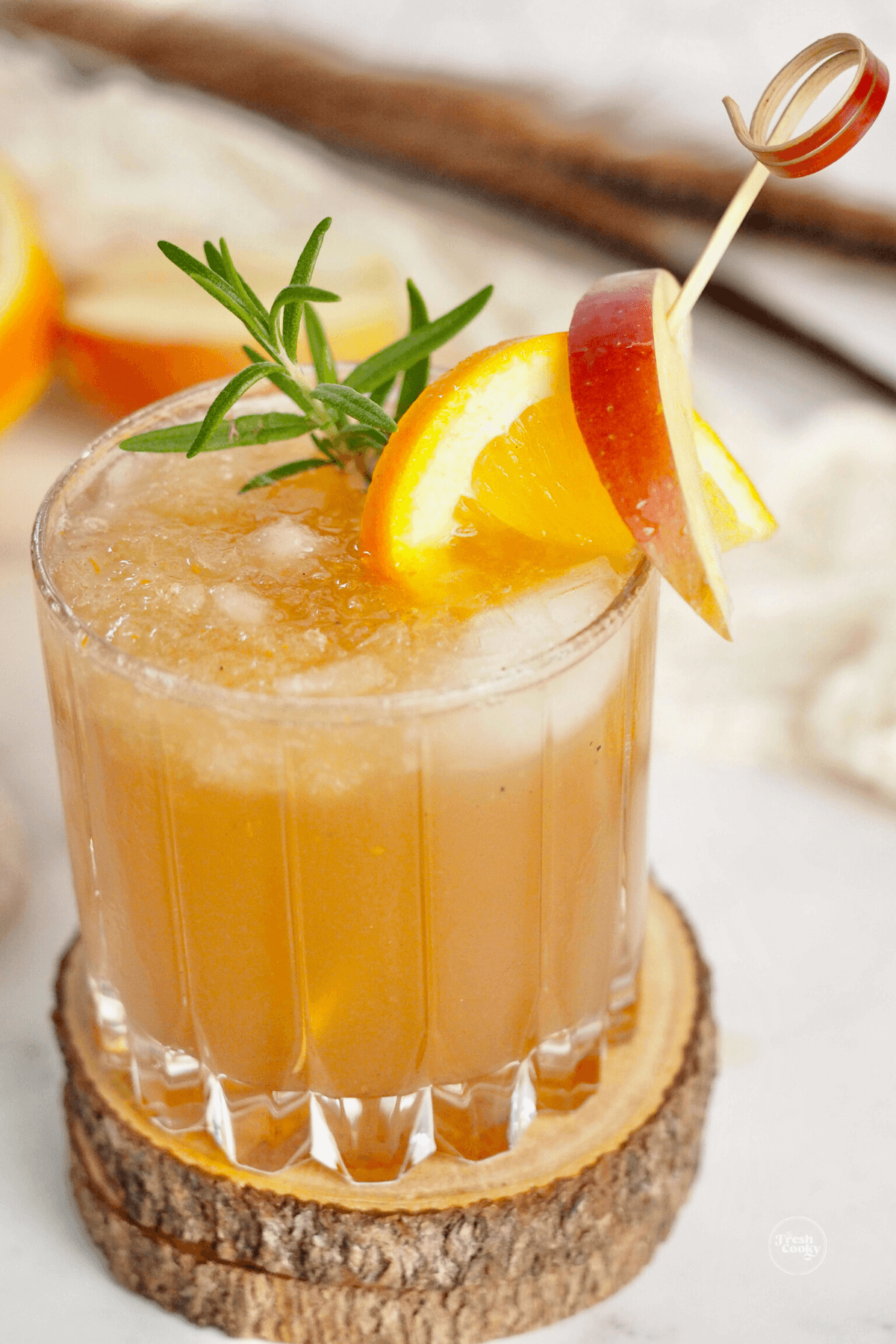 Apple cider bourbon smash in pretty cocktail glass with pick filled with apples, orange and a sprig of rosemary.
