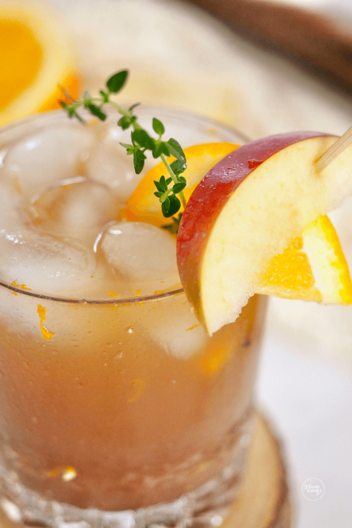 Apple Cider bourbon cocktail close-up in old-fashioned glass with sprig of thyme and fresh apple and orange.