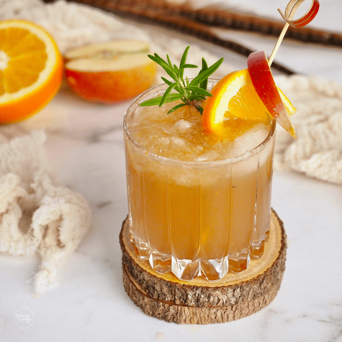 Apple Cider Bourbon cocktail in pretty glass with garnish of apple, orange and rosemary.