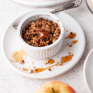 Bowl filled with apple crisp drizzled with maple syrup.
