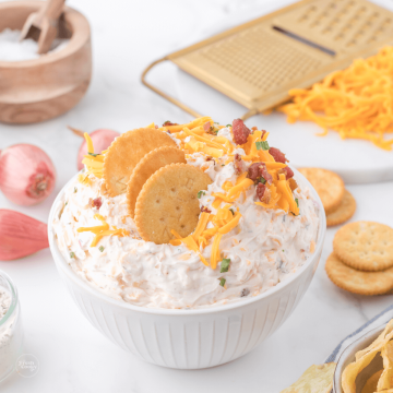 Cowboy crack dip in bowl with shredded cheddar behind and ritz crackers.