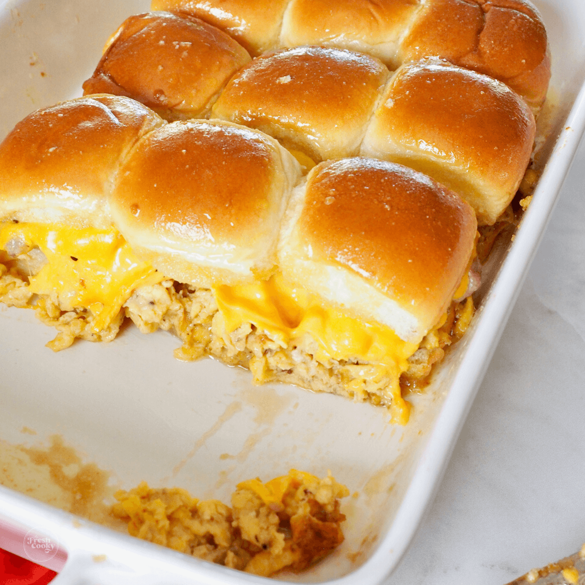 Egg sandwiches sliders in a baking dish with melty cheese.