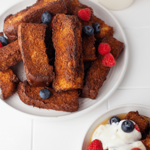 Air fryer french toast sticks on plate with berries.