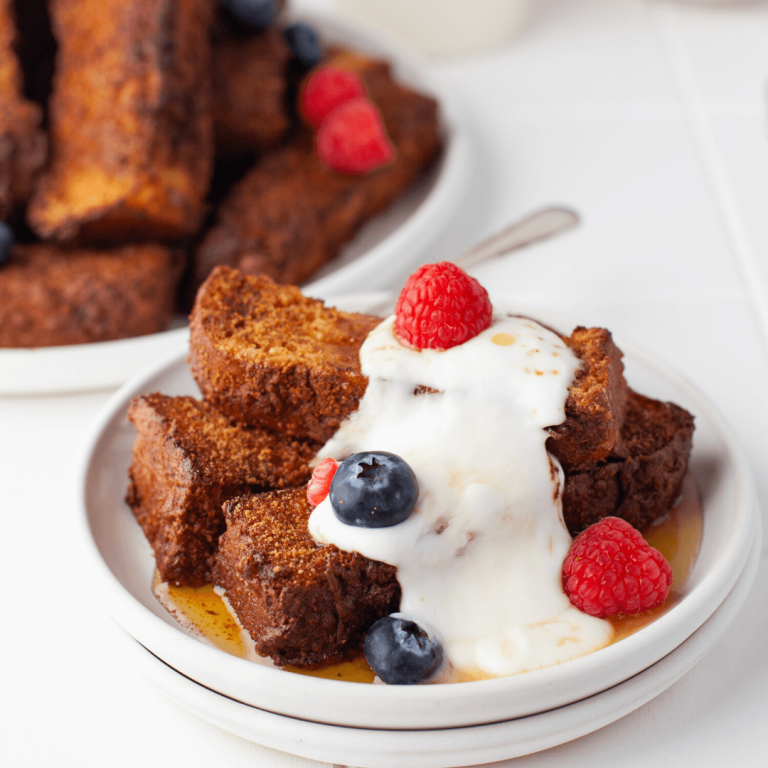 Air fried cinnamon sugar french toast sticks on plate with a little cream and berries.