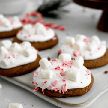 Hot cocoa mix cookies on platter topped with marshmallow fluff, mini marshmallows and crushed candy canes.