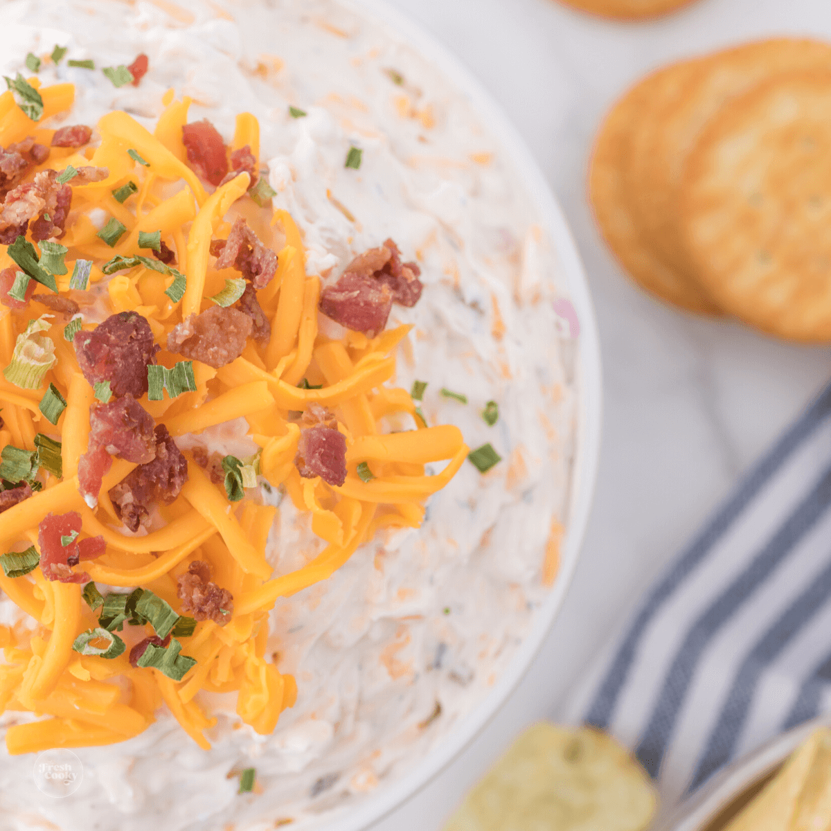 Cowboy crack dip in small bowl topped with cheddar cheese and bacon bits.
