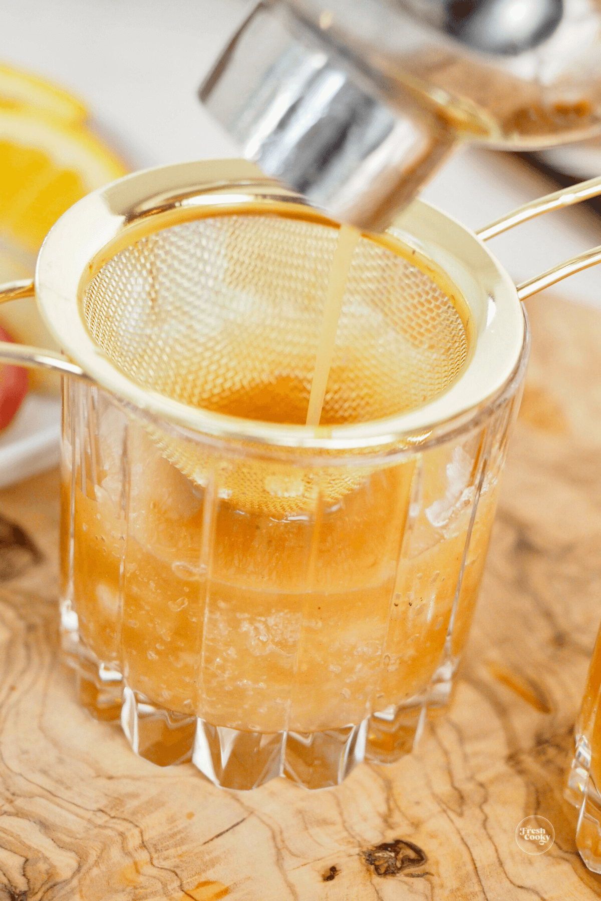 Adding apple cider cocktail mixture to glass through a strainer. 
