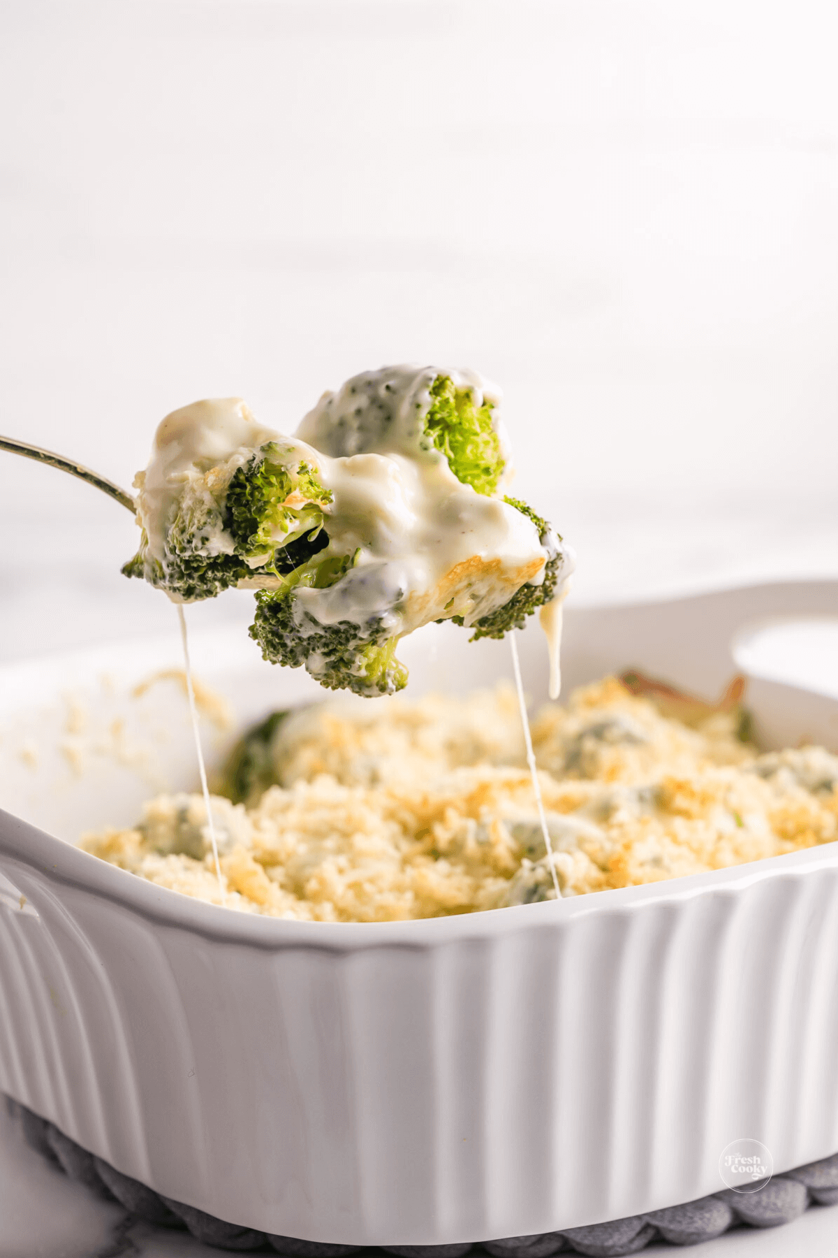 Spoon serving cheesy broccoli au gratin..