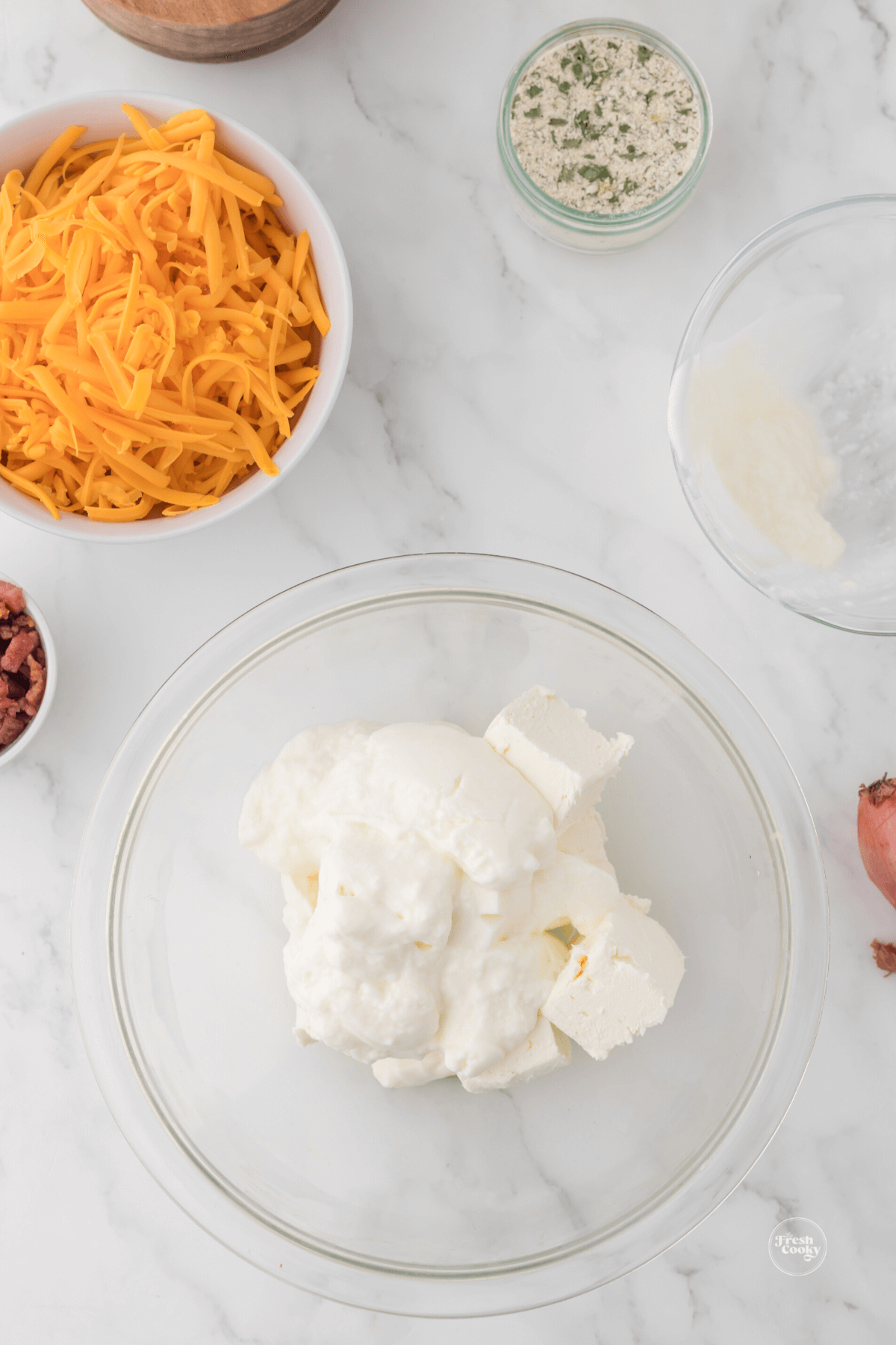 Sour cream and cream cheese in bowl with shredded cheese behind. 