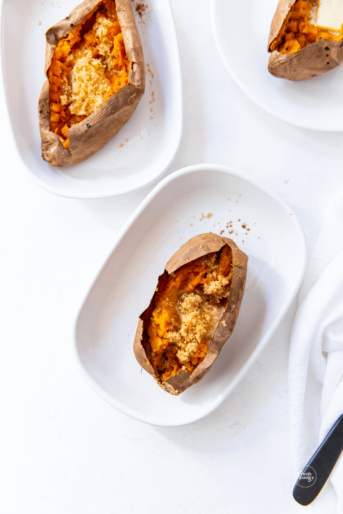 Baked sweet potatoes on plates with variety of toppings.