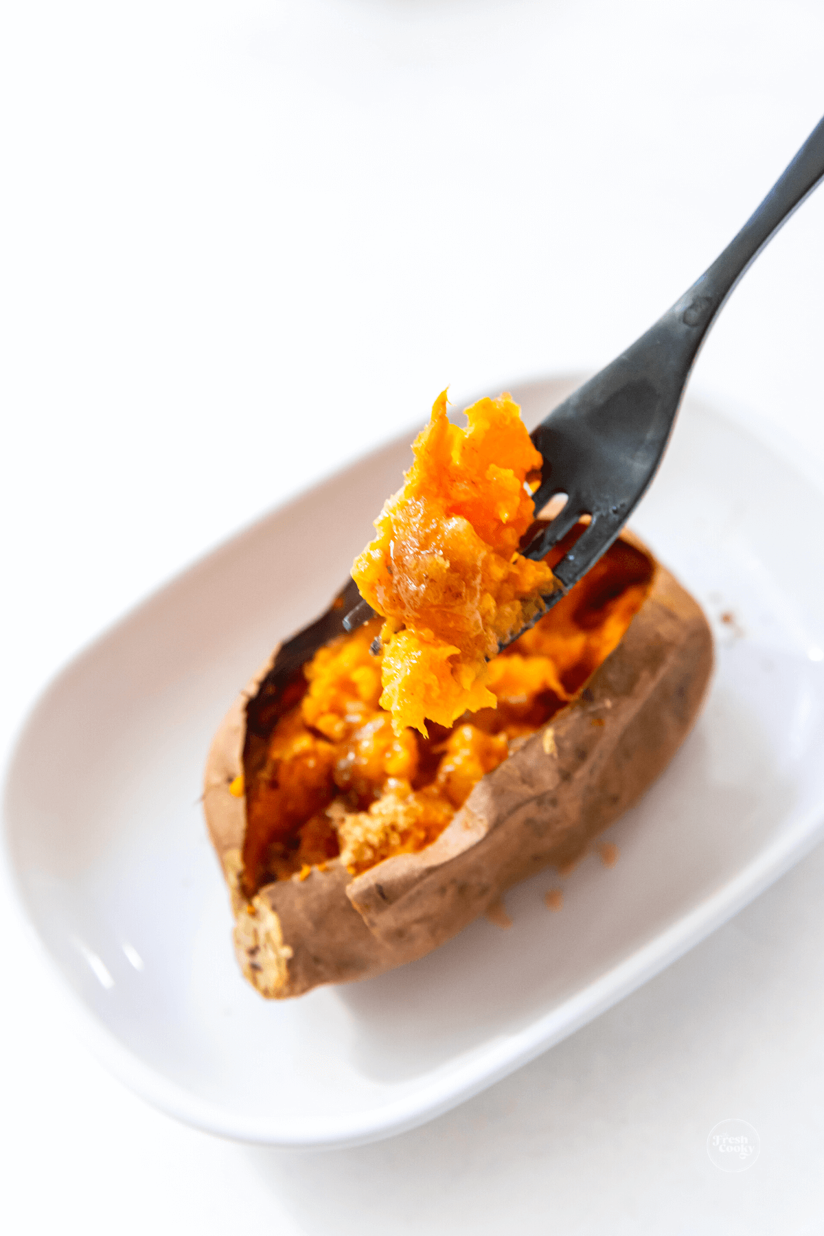 Easy healthy air fryer baked sweet potato on plate with forkful of potato flesh.