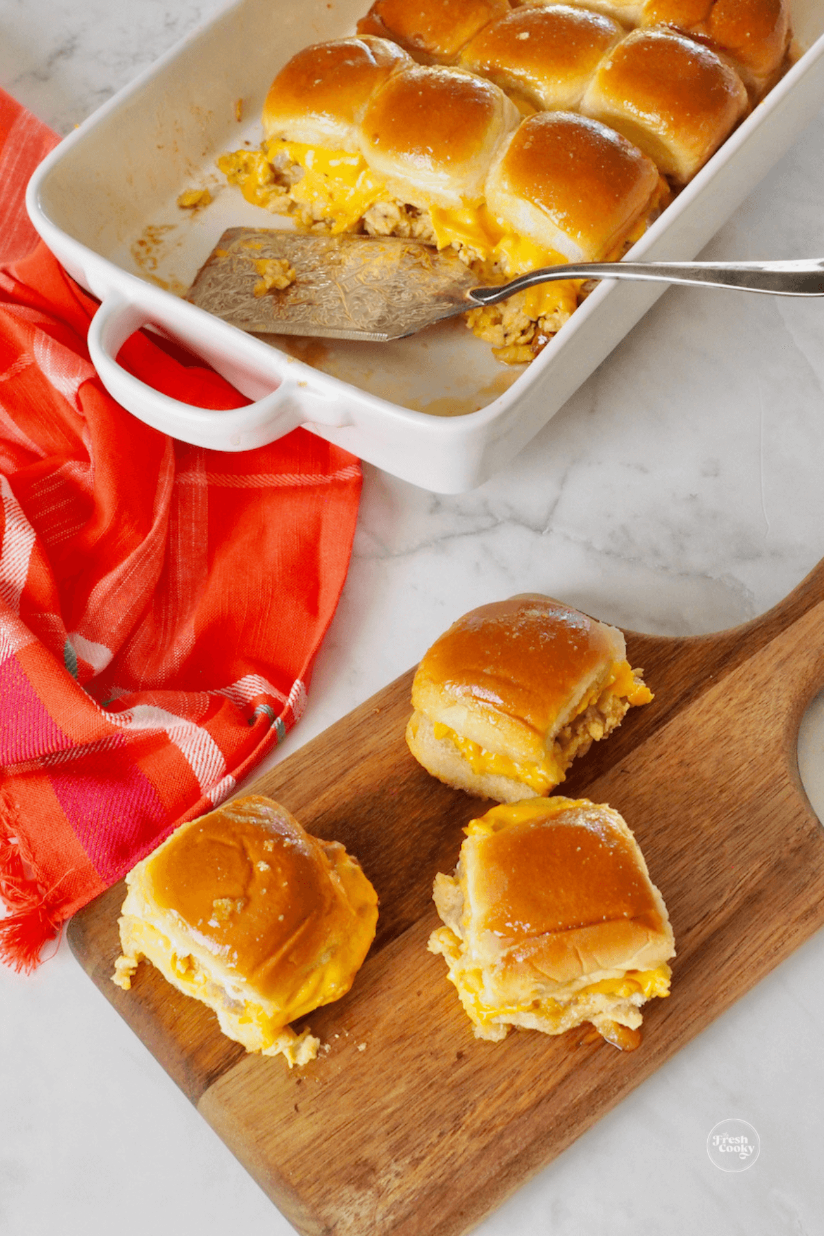 Breakfast sliders on wooden cutting board with the rest in pan with spatula.