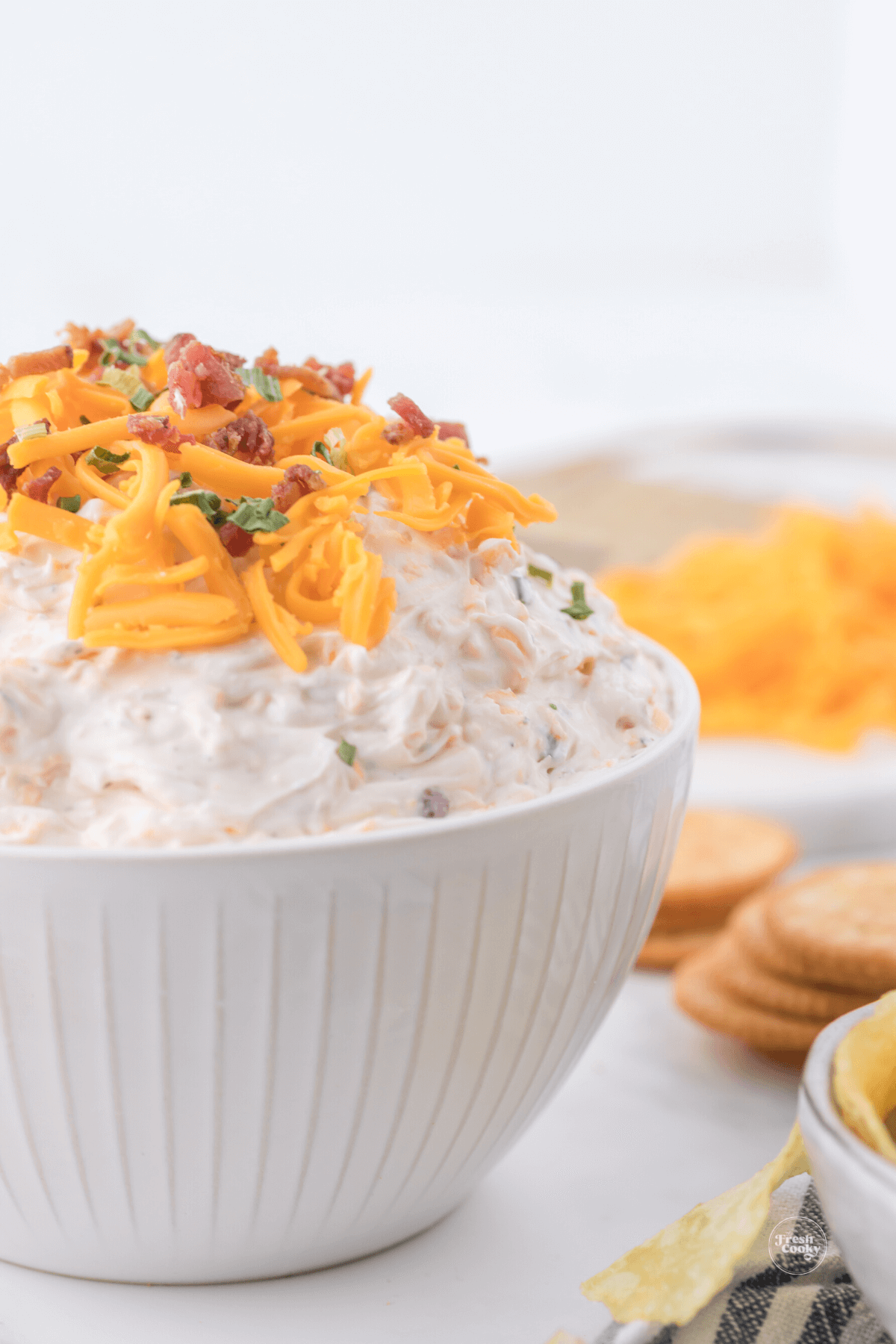 Cowboy crack dip recipe in pretty white bowl with crackers and shredded cheese in background.