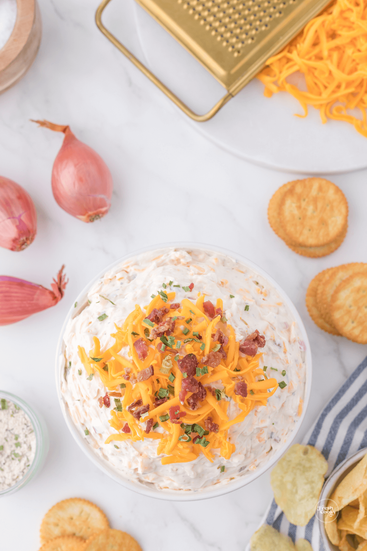 Looking at a cheesy, creamy dip topped with shredded cheddar and bacon bits. 