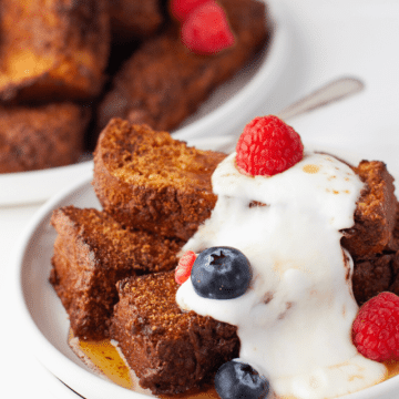 Air fried cinnamon sugar french toast sticks on plate with a little cream and berries.