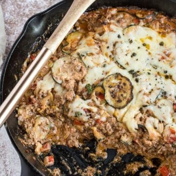 Zucchini Ground Beef Casserole cooked in a skillet with a wooden spoon and one missing serving.