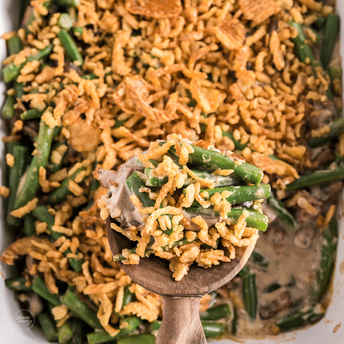 Creamy, ultimate green bean casserole with serving on wooden spoon. 