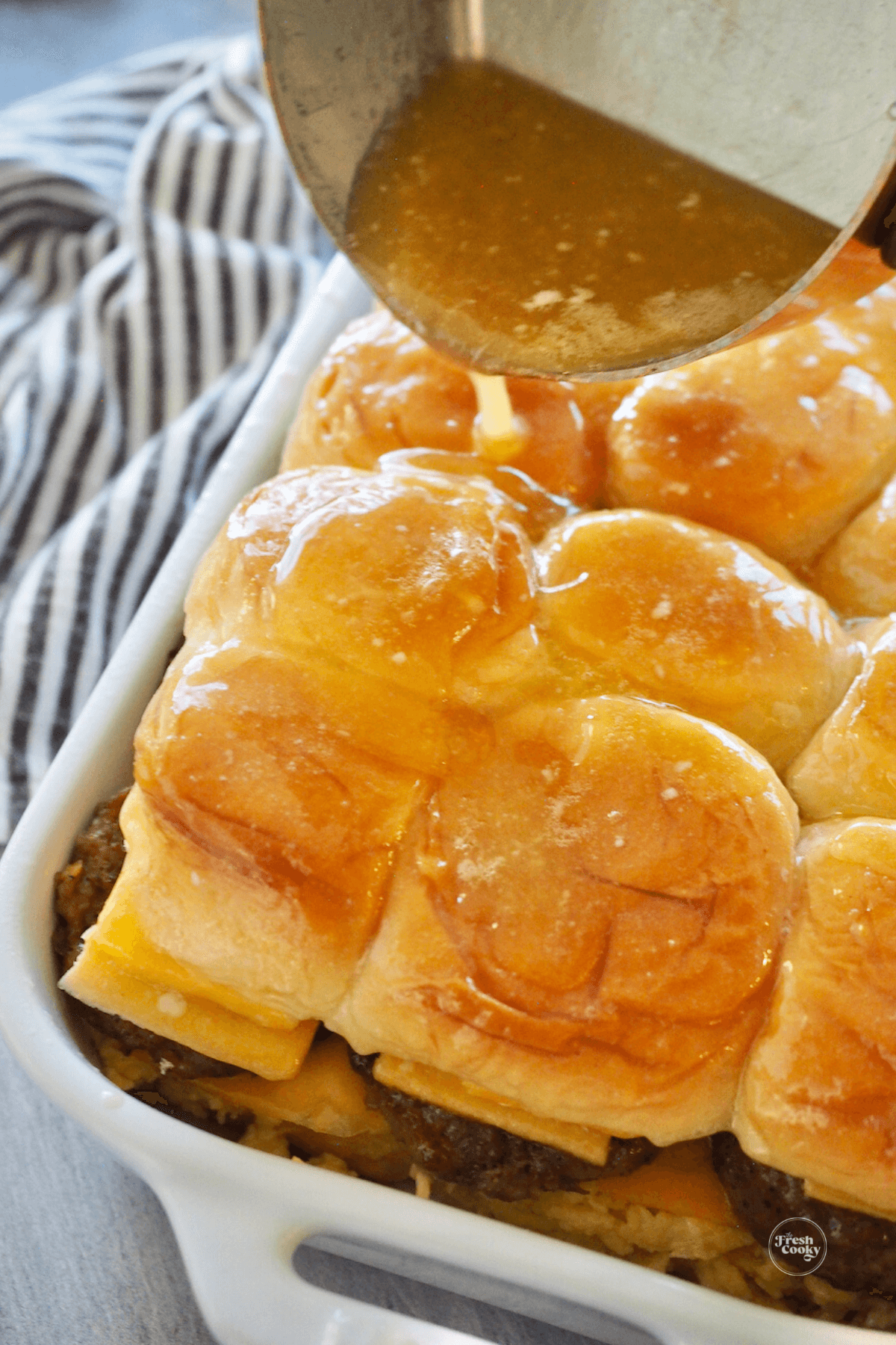 Pouring maple syrup butter over the slider rolls. 