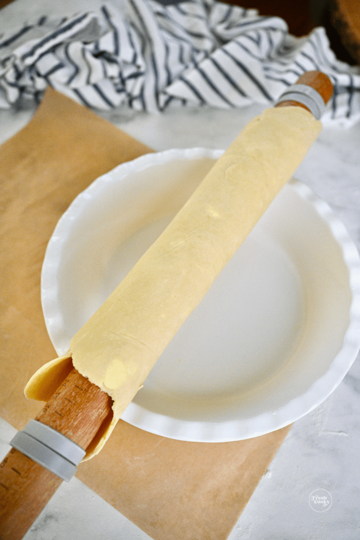 Using rolling pin to roll pie dough onto plate.