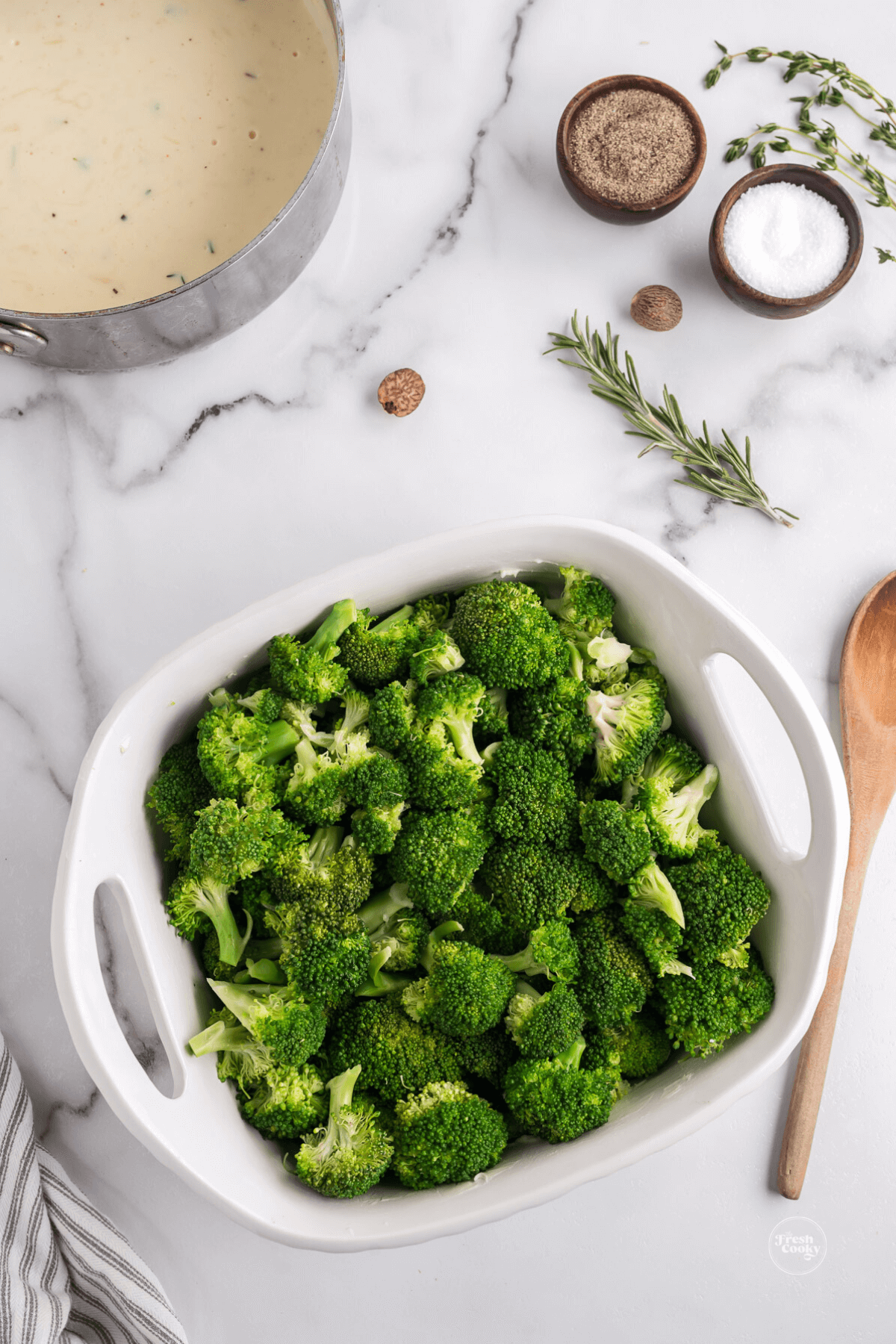 Steamed broccoli in baking dish with white sauce nearby. 
