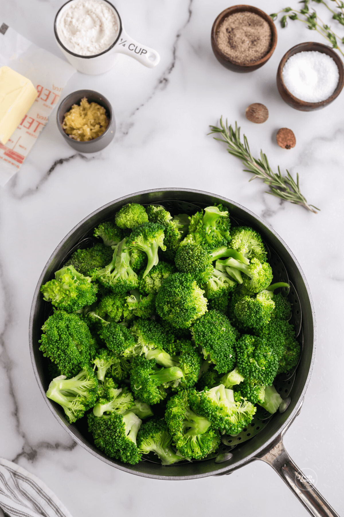 Steamed broccoli in pot with ingredients for au gratin beside.