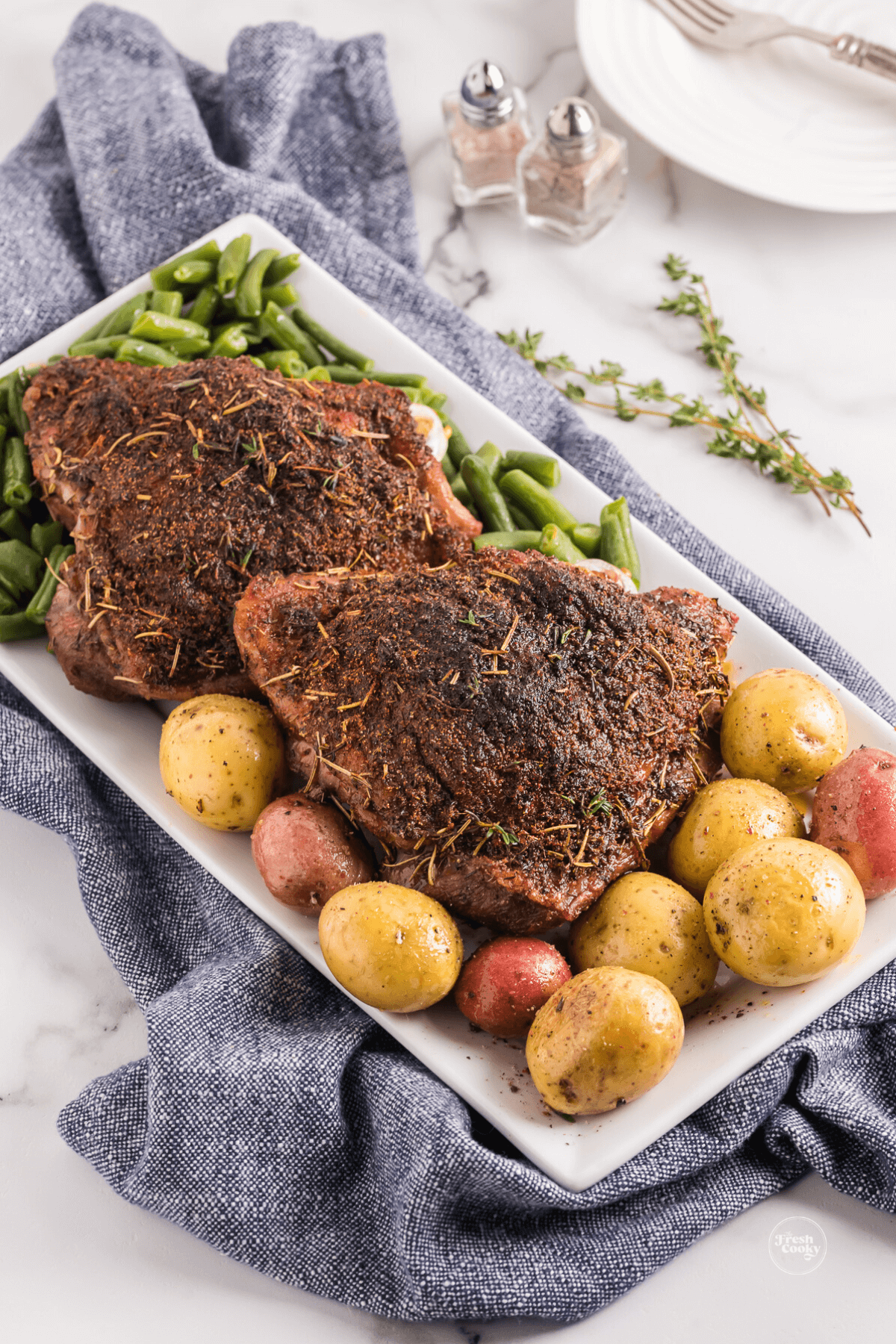 Two turkey thighs surrounded by potatoes and green beans.