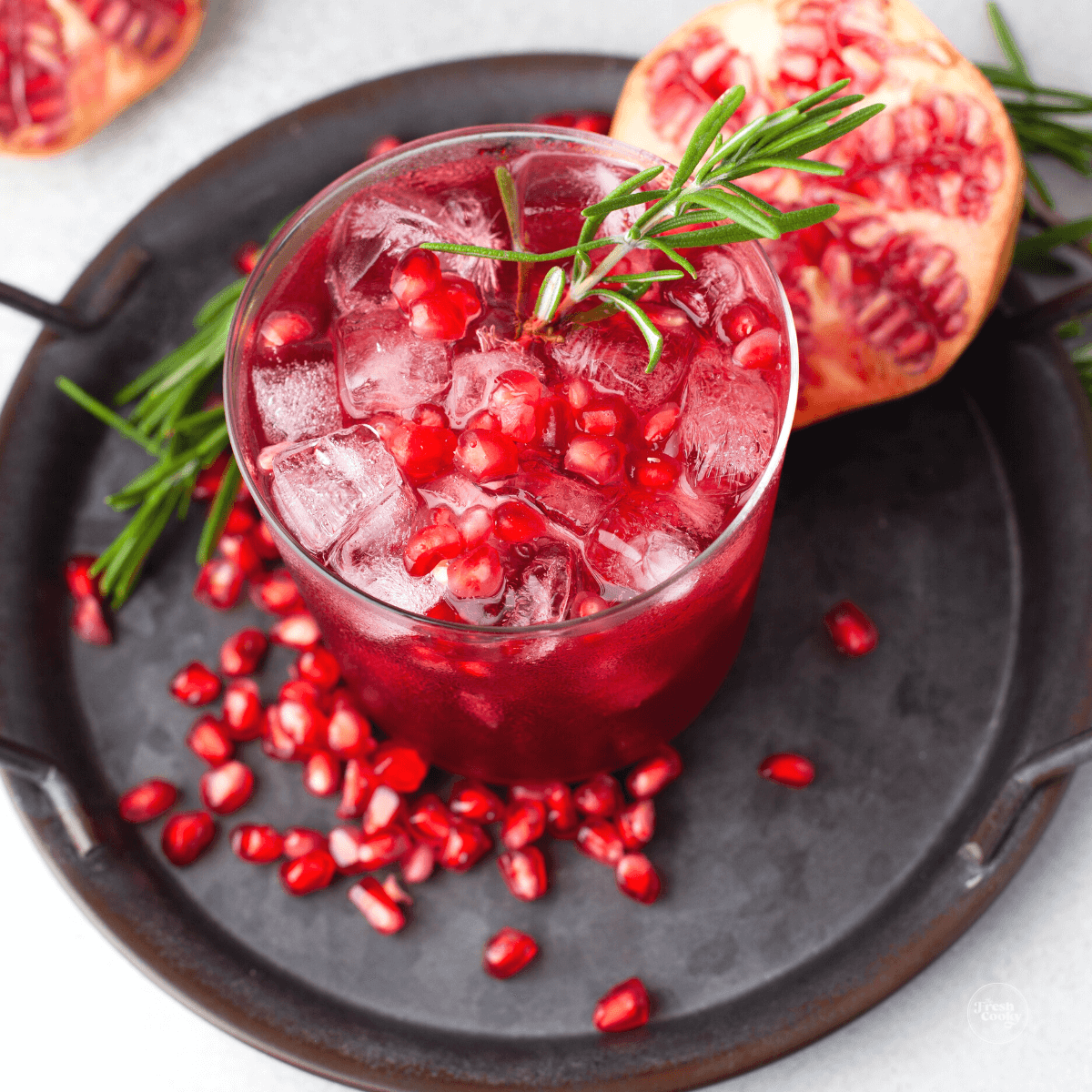 Christmas margarita in a glass with pomegranate arils and some fresh rosemary.