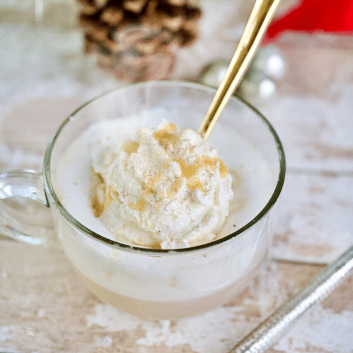 Mug of Christmas Morning Chai latte in a glass mug topped with whipped cream and nutmeg and drizzled with white chocolate sauce.