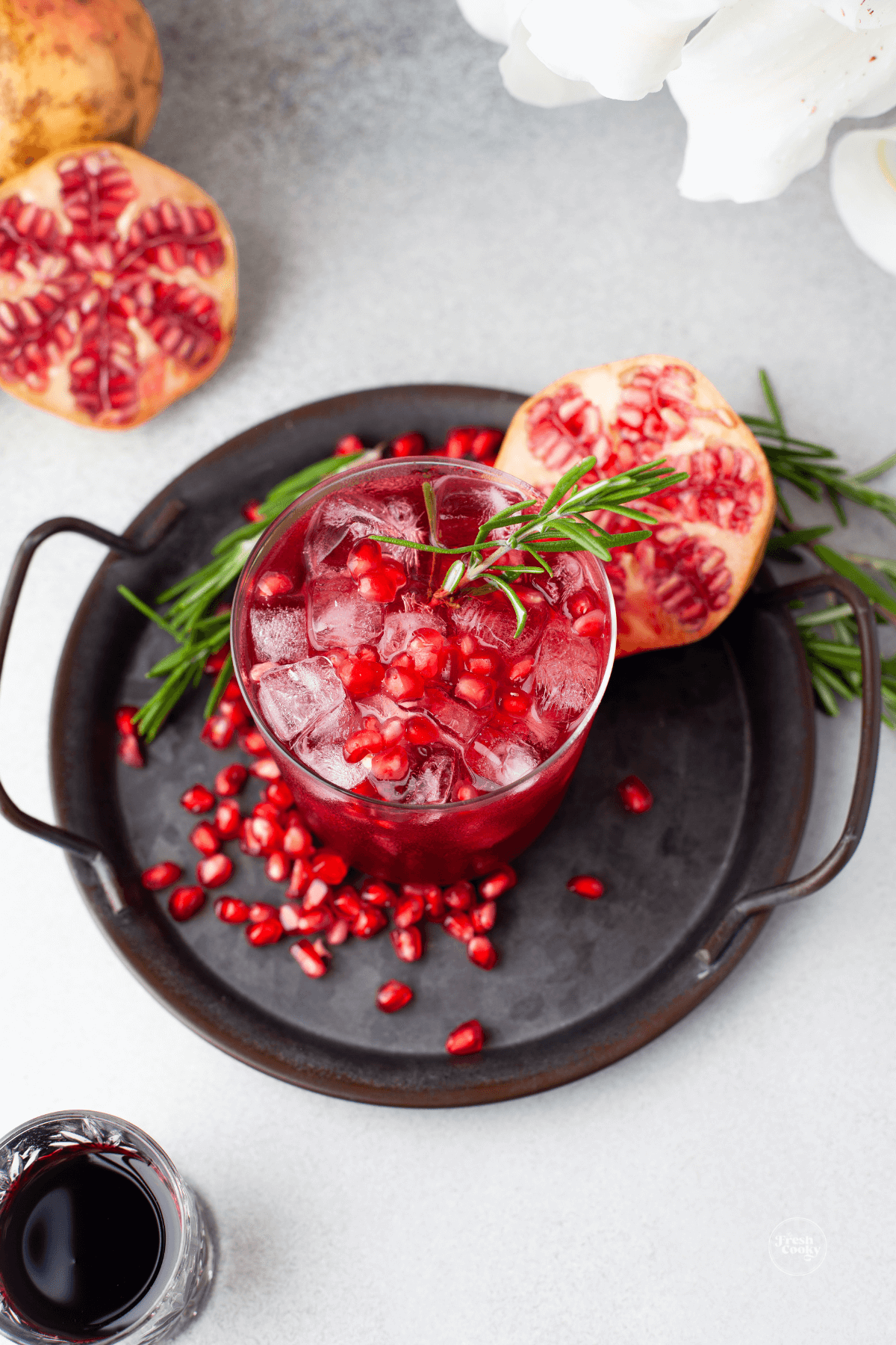 Mistletoe Margarita in pretty glass on black tray garnished with rosemary and fresh pomegranate arils.