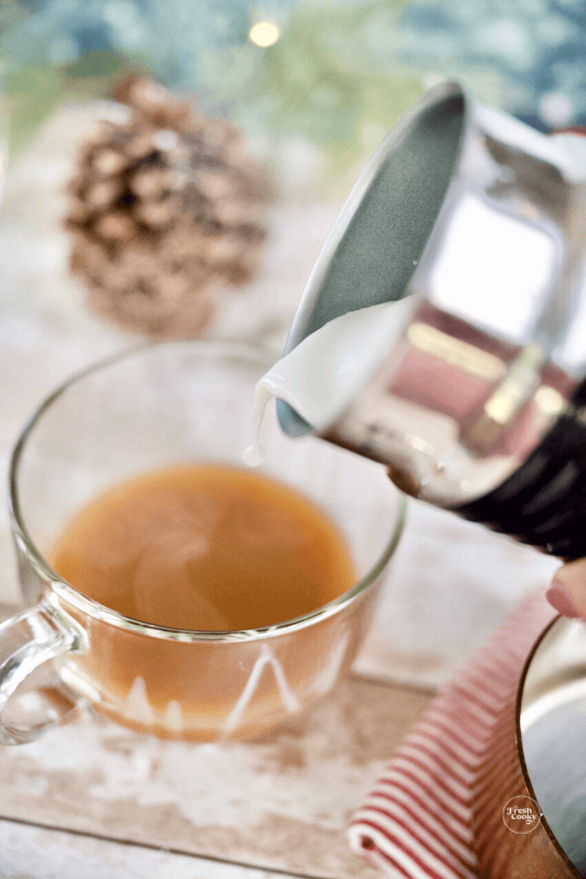 Pouring foamed and steamed half and half into mug with chai tea.
