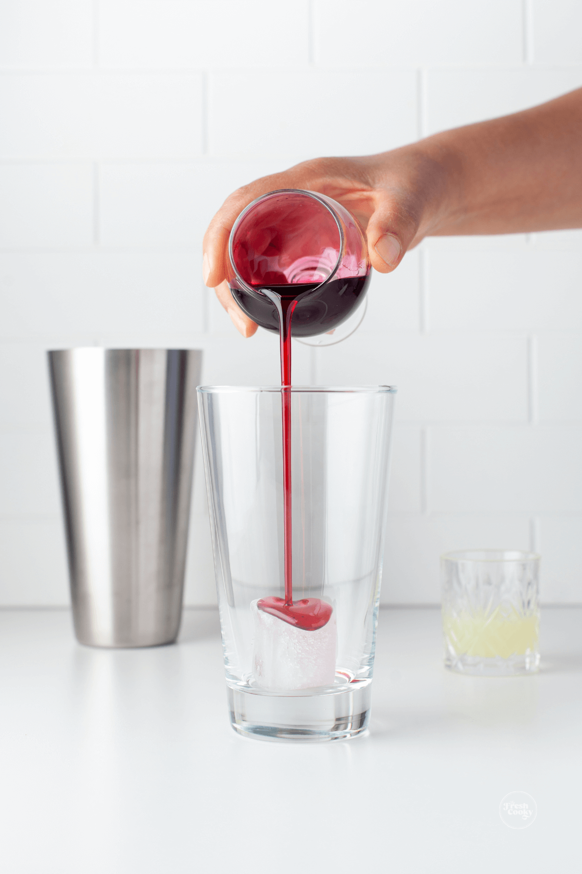 Pouring hibiscus pomegranate syrup into ice filled cocktail shaker. 