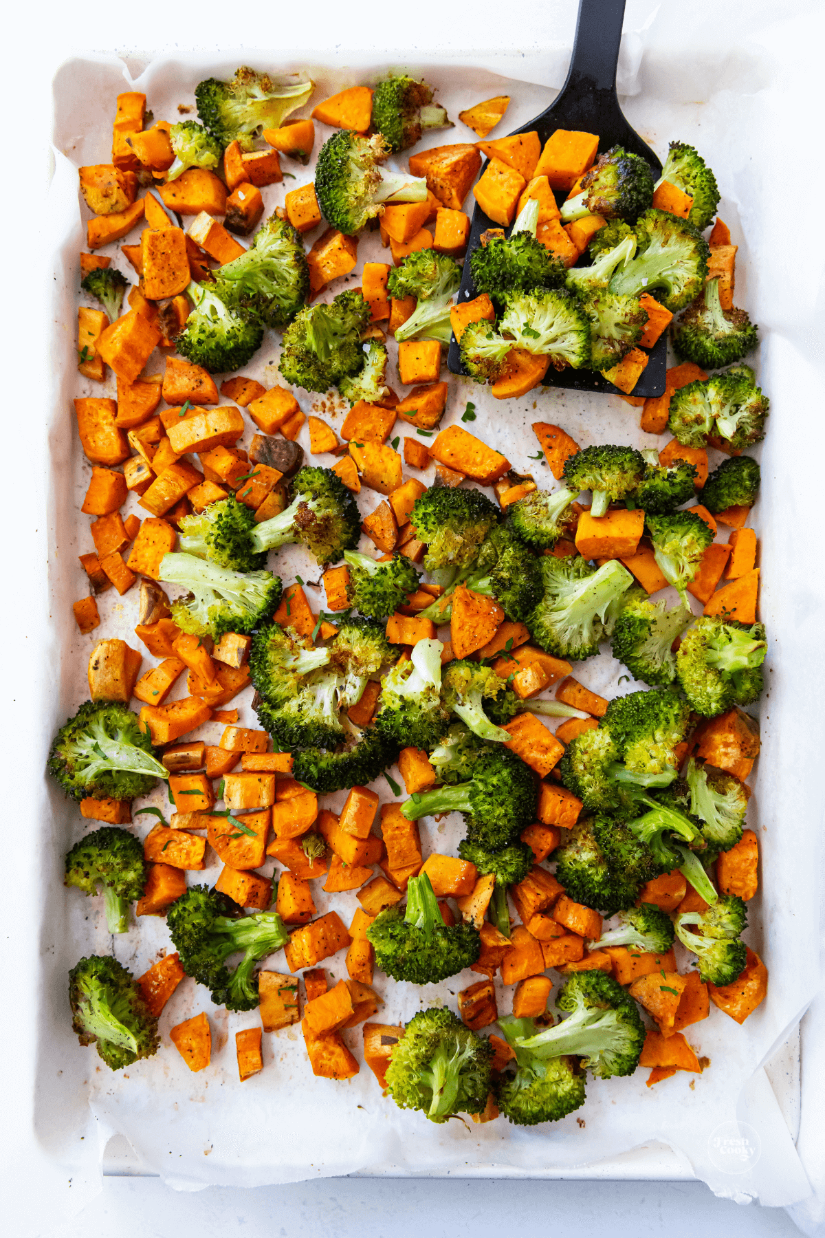 Easy roasted sweet potatoes and broccoli on sheet pan with spatula removing some. 