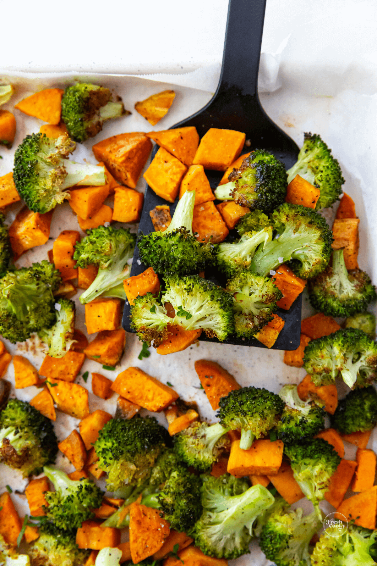 Roasted sweet potatoes and broccoli on sheet pan with spatula.