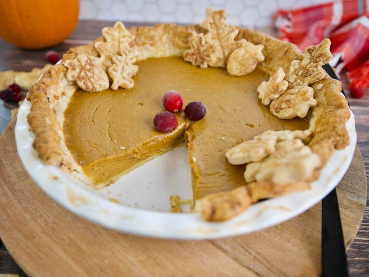 Costco pumpkin pie with slice removed and cranberries on top.