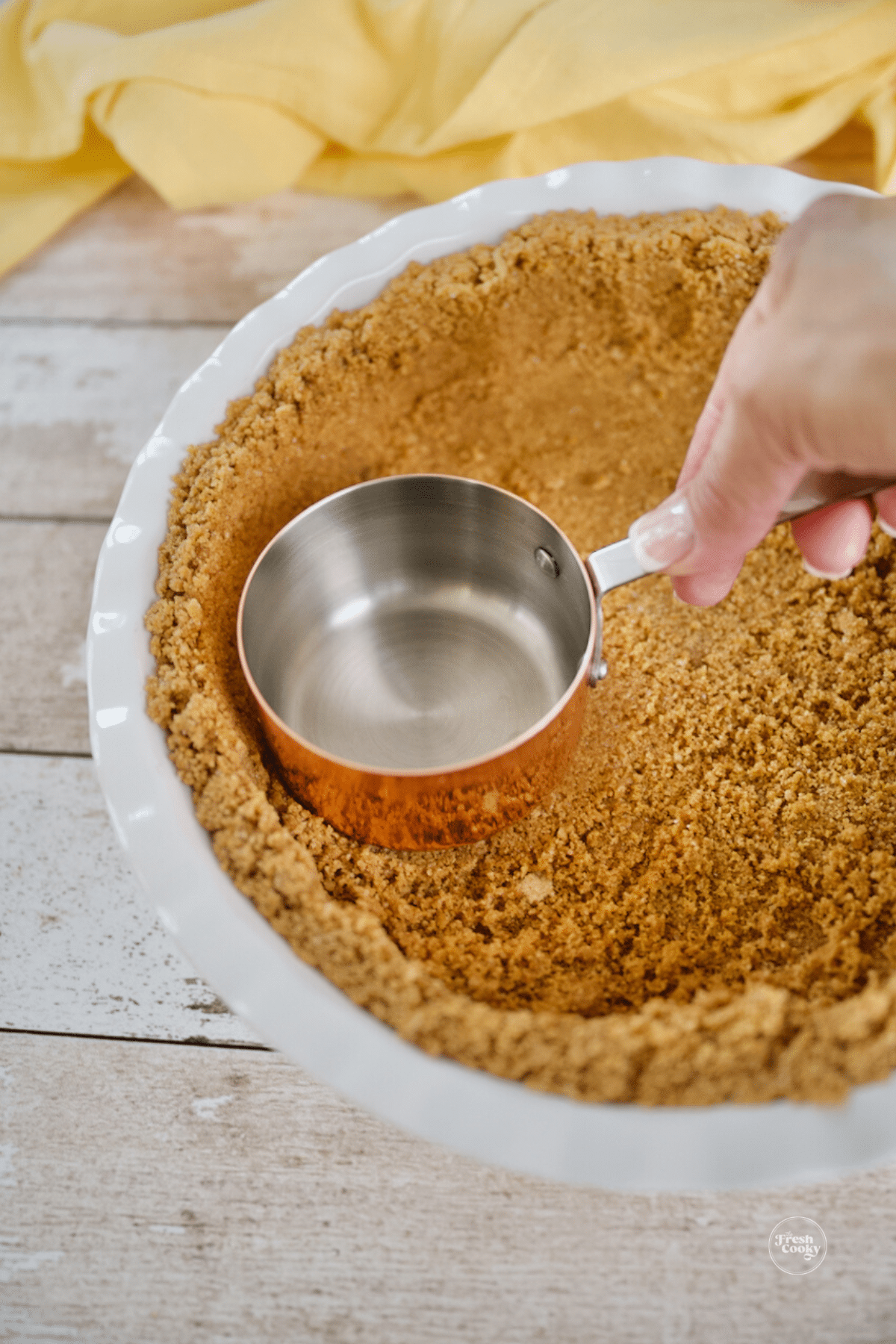 Using measuring cup to firmly press mixture into bottom and sides of pie dish. 