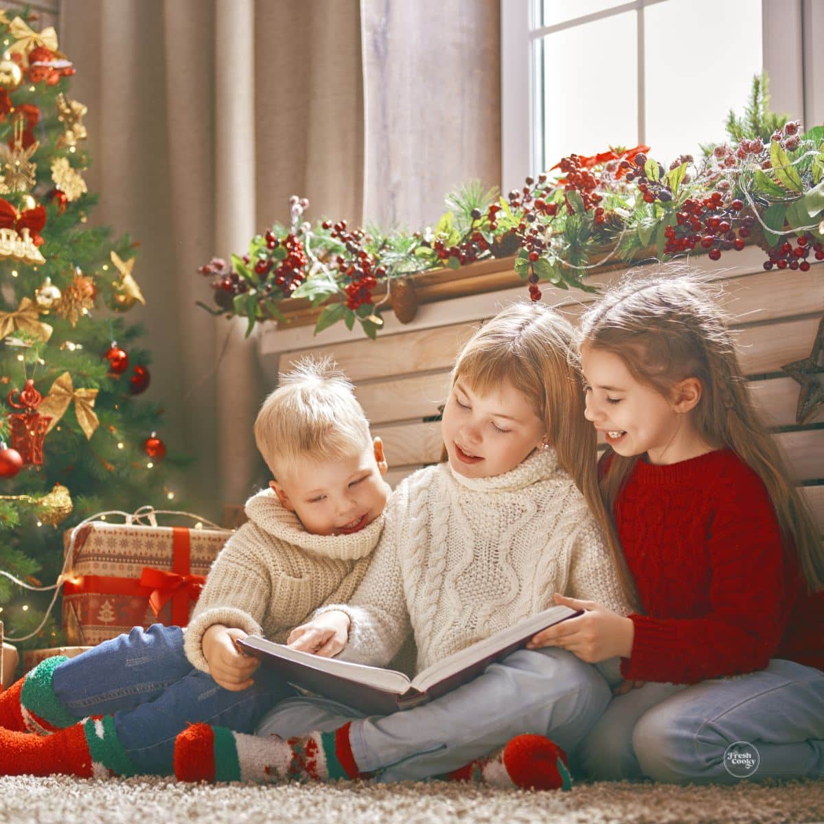 Three siblings sitting near the Christmas tree reading an advent book.