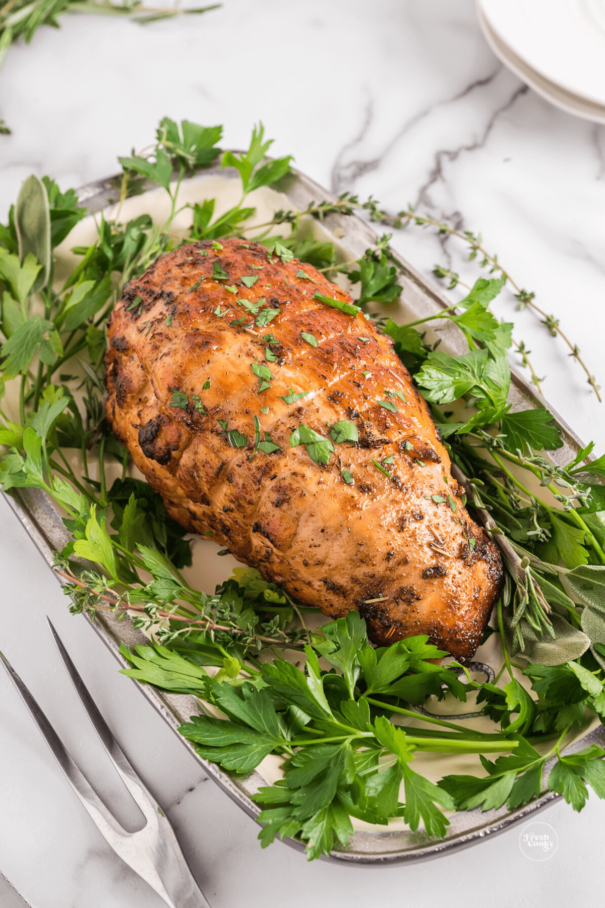 Whole cooked turkey breast on platter with greens surrounding it, before carving.