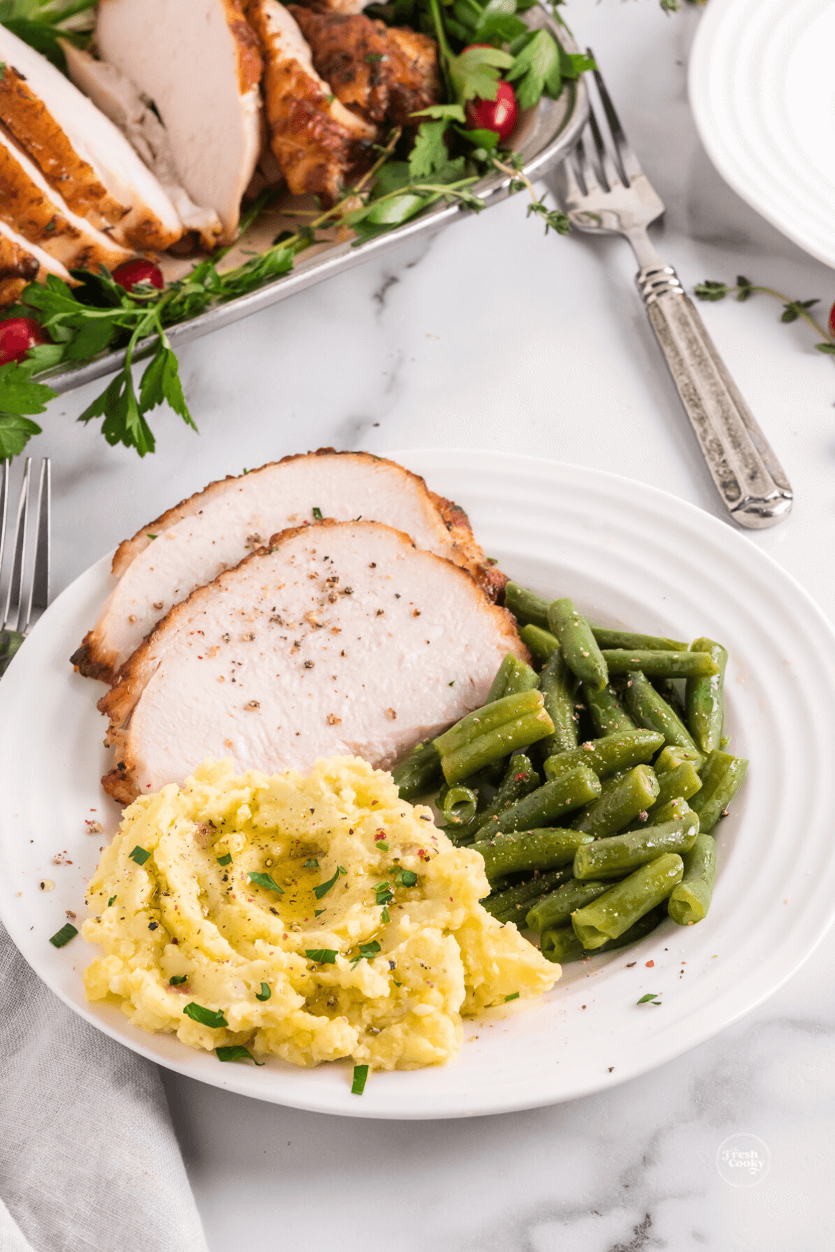 Plate of boneless turkey breast sliced with mashed potatoes and green beans.