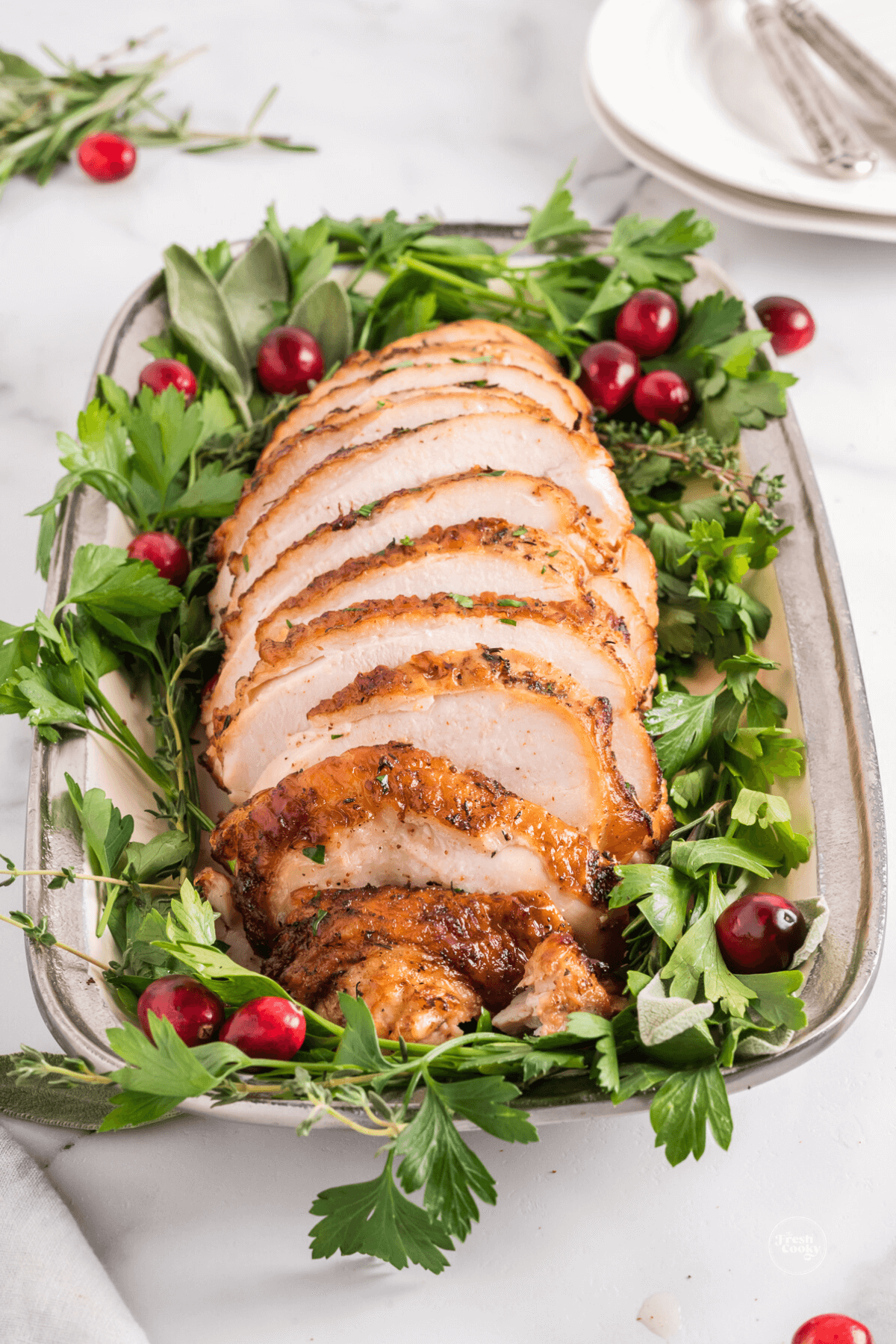 Sliced turkey breast on a holiday tray with cranberries and fresh herbs. 