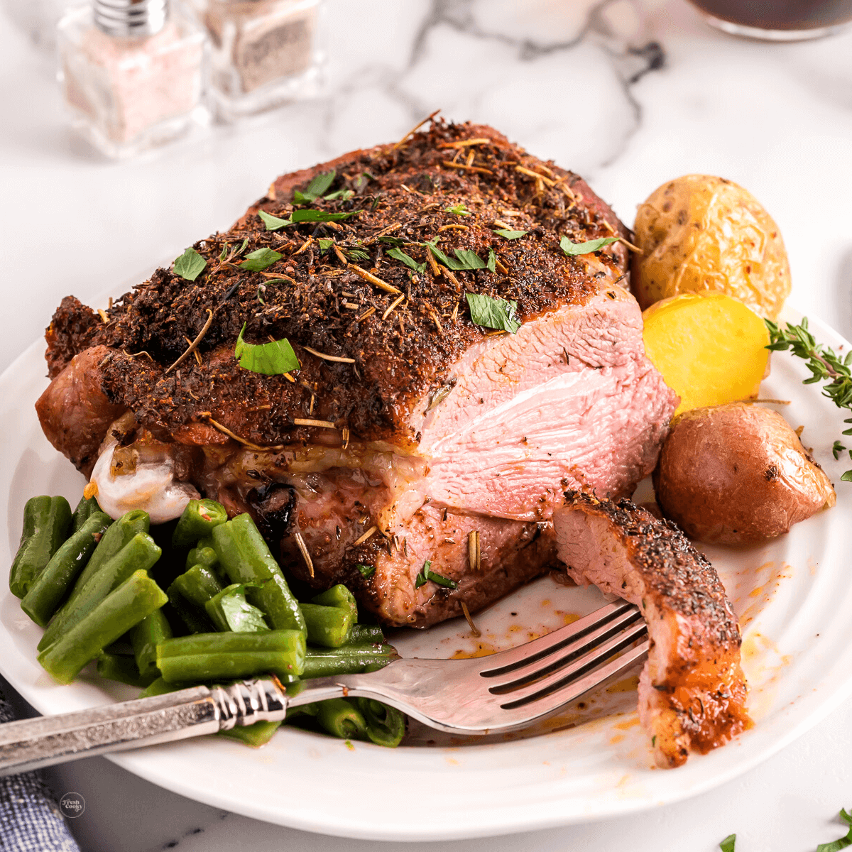 Sliced air fryer turkey thigh on plate with green beans and potatoes.