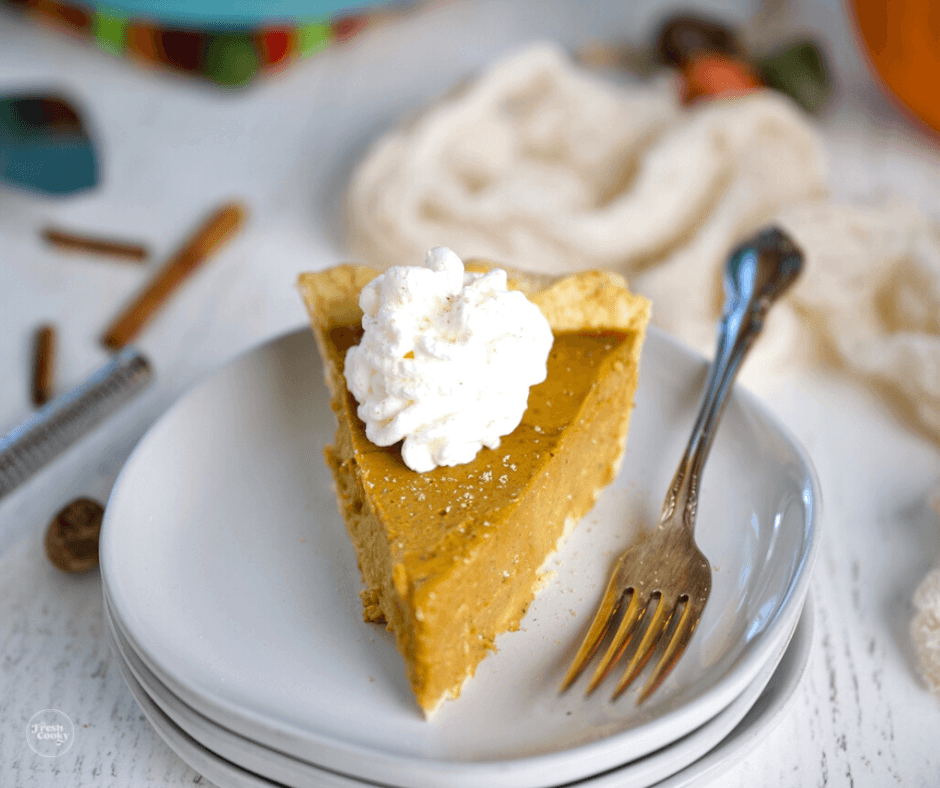 pumpkin custard pie slice on plate with swirl of whipped cream.