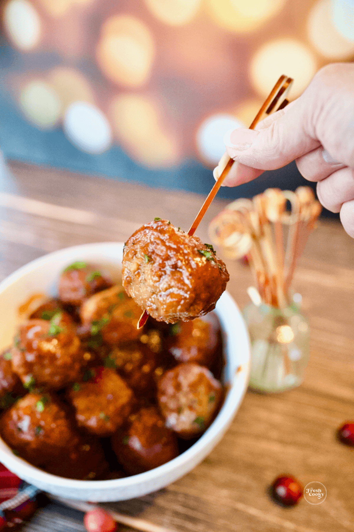 Three ingredient cranberry meatballs with hand holding a meatball on a cocktail stick.